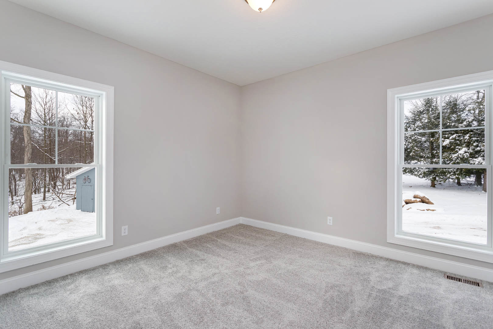 Carpeted room with white walls, two large windows overlooking snowy trees, simple baseboard molding
