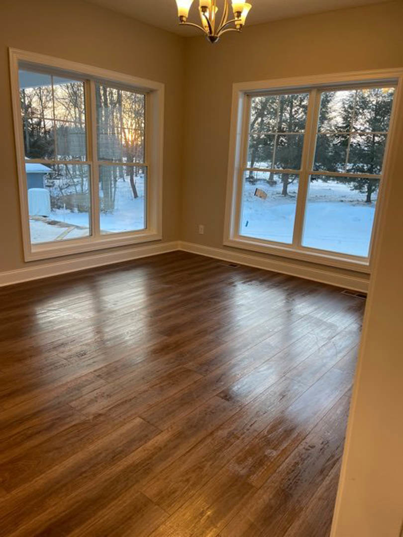 Wood floor room featuring large windows with snowy yard views, white walls, and a modern chandelier.