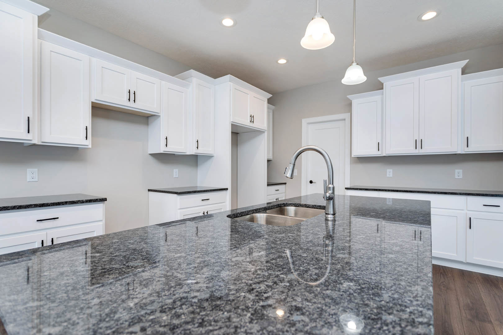 White shaker cabinets and granite countertops in a kitchen with stainless steel sink, chrome faucet, tile backsplash, and built-in appliances