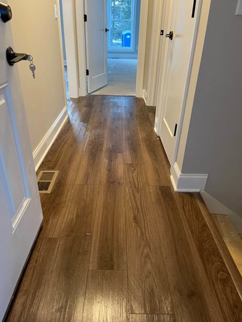 Hallway with wood flooring, white doors featuring black handles, wall vent, and an open door revealing a window.