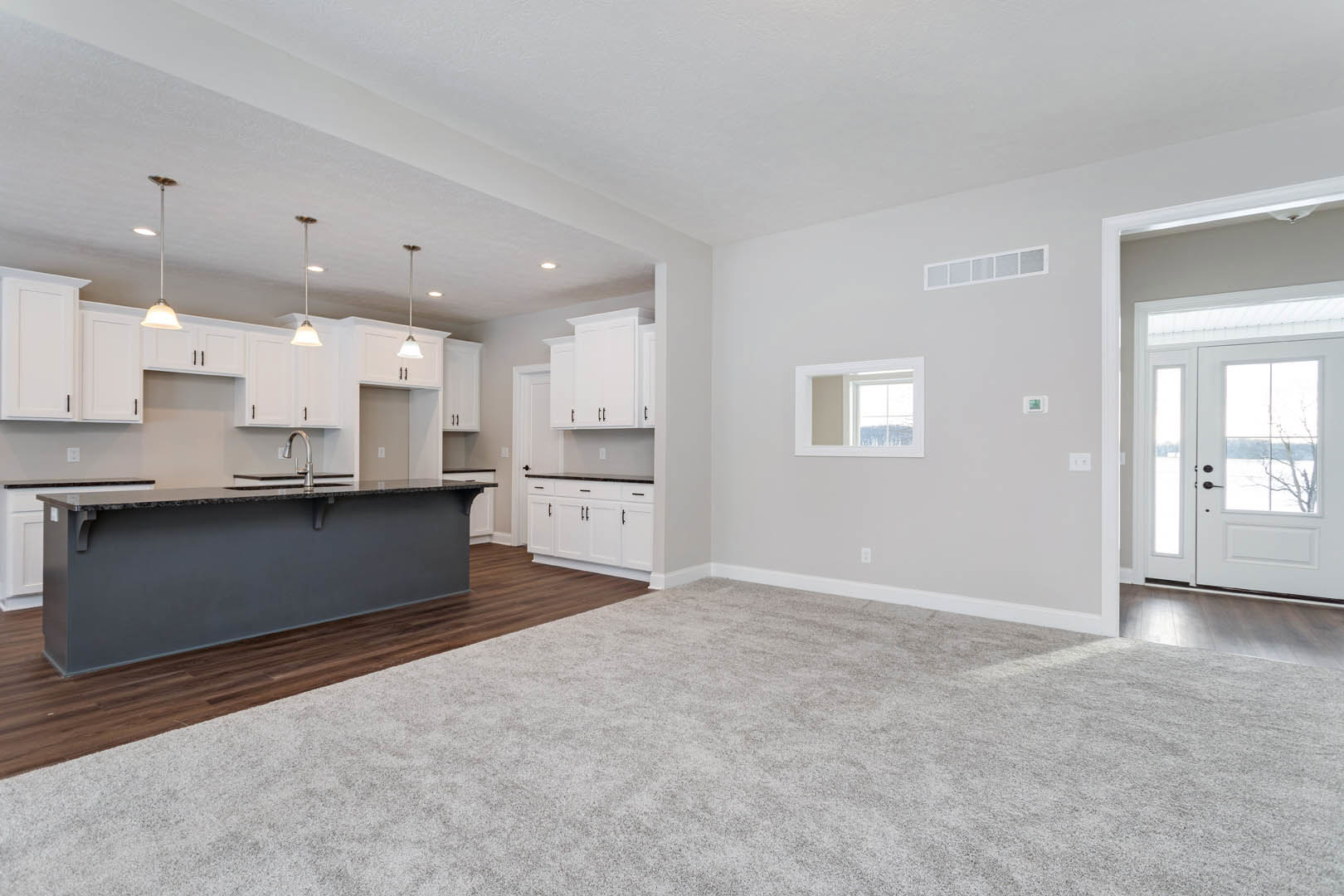 Open kitchen and living room with light carpet flooring, white cabinetry, stone countertop, stainless sink, and a white door with glass panes.