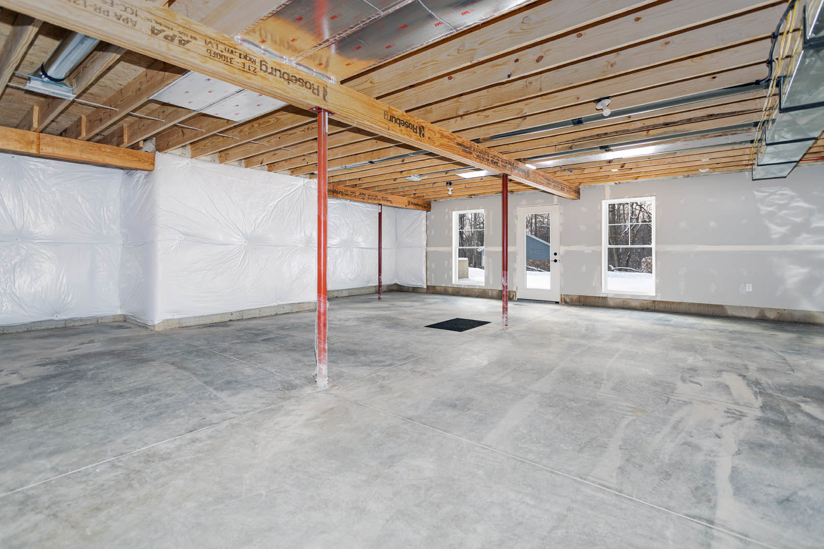Concrete floor with exposed wooden ceiling beam, red structural pole, white walls, and large window overlooking forest.