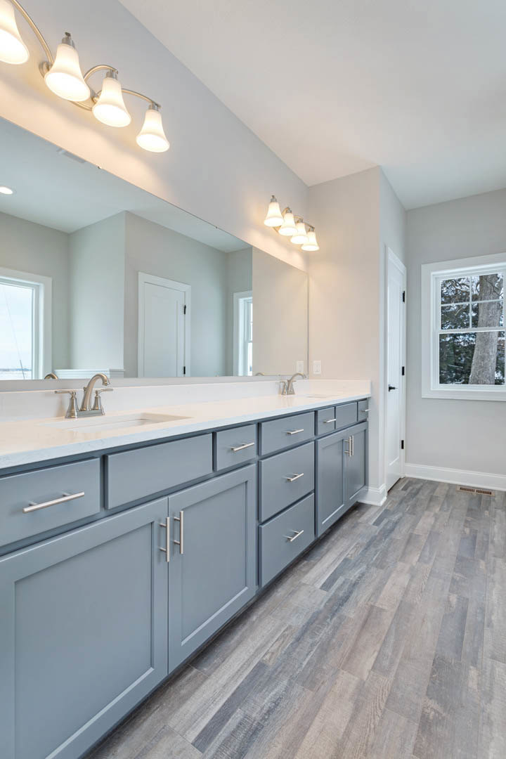 Bathroom with expansive mirror above gray shaker cabinets, quartz countertop, chrome faucet, and window framing leafy tree outside