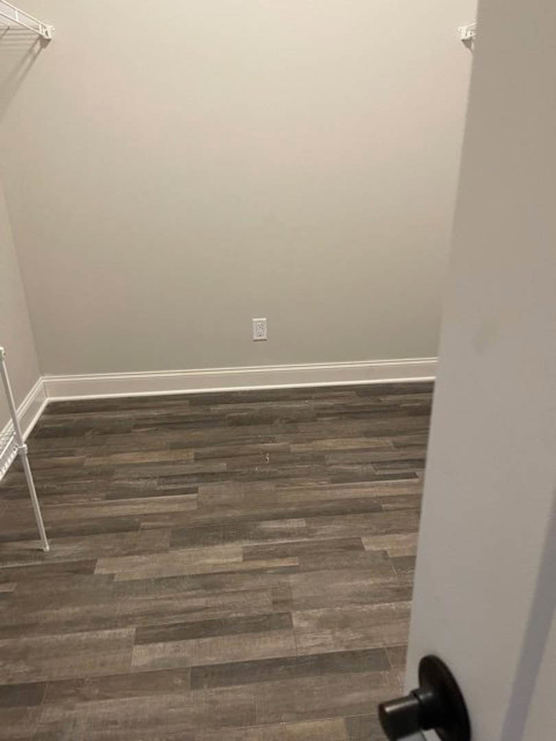 Light wood flooring in a room with white plaster walls, black accent stripe, and a close-up of a silver door knob on a white door
