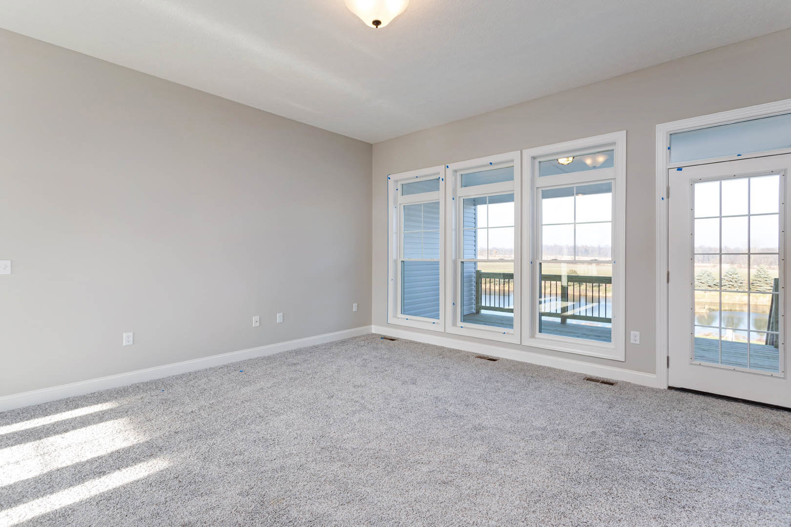 Carpeted living area with large windows and glass door opening to a deck, white walls, crown molding, and view of trees outside