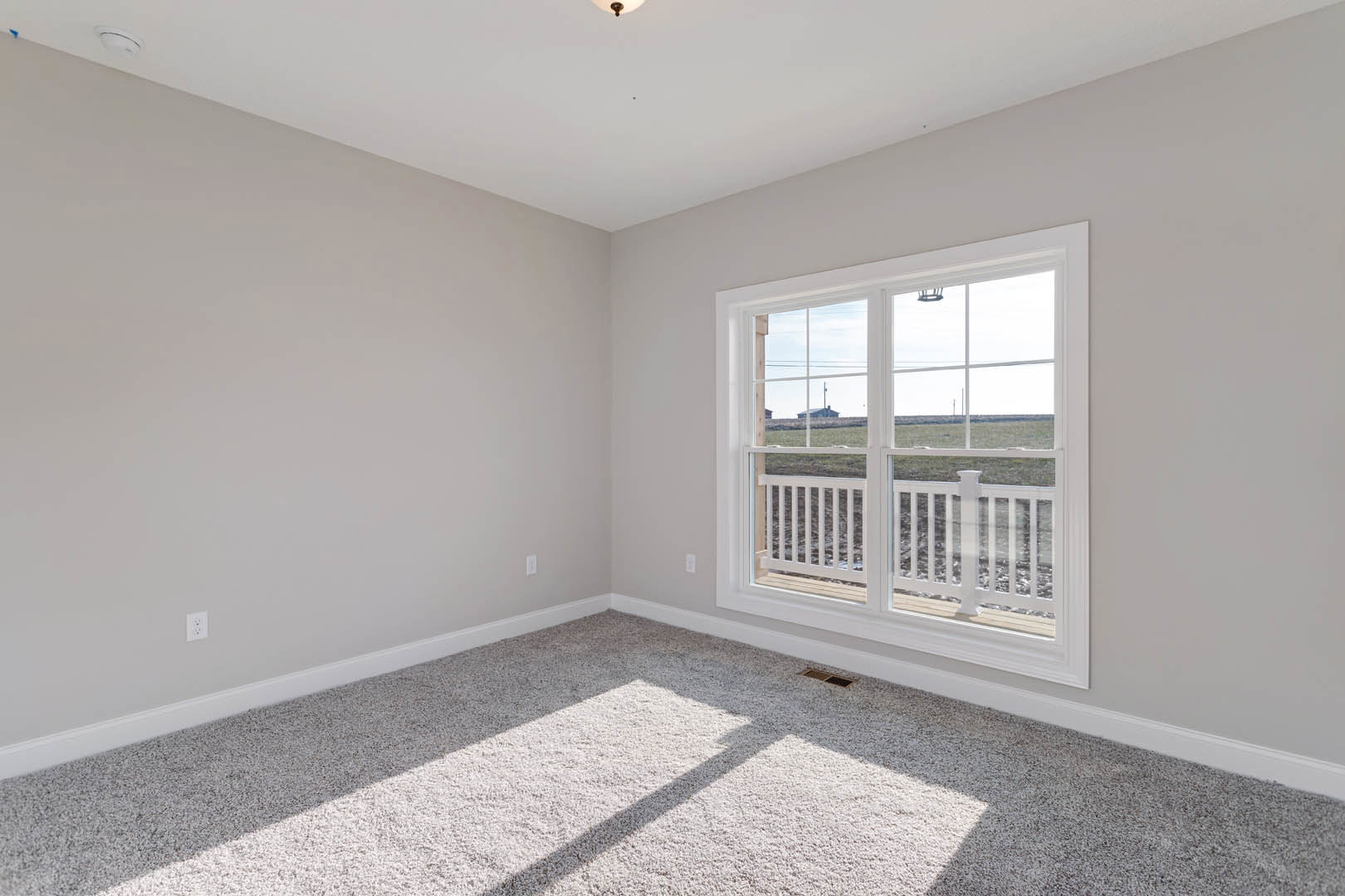 Bright room with white carpet, large window overlooking grassy field, white walls, and close-up of white railing.