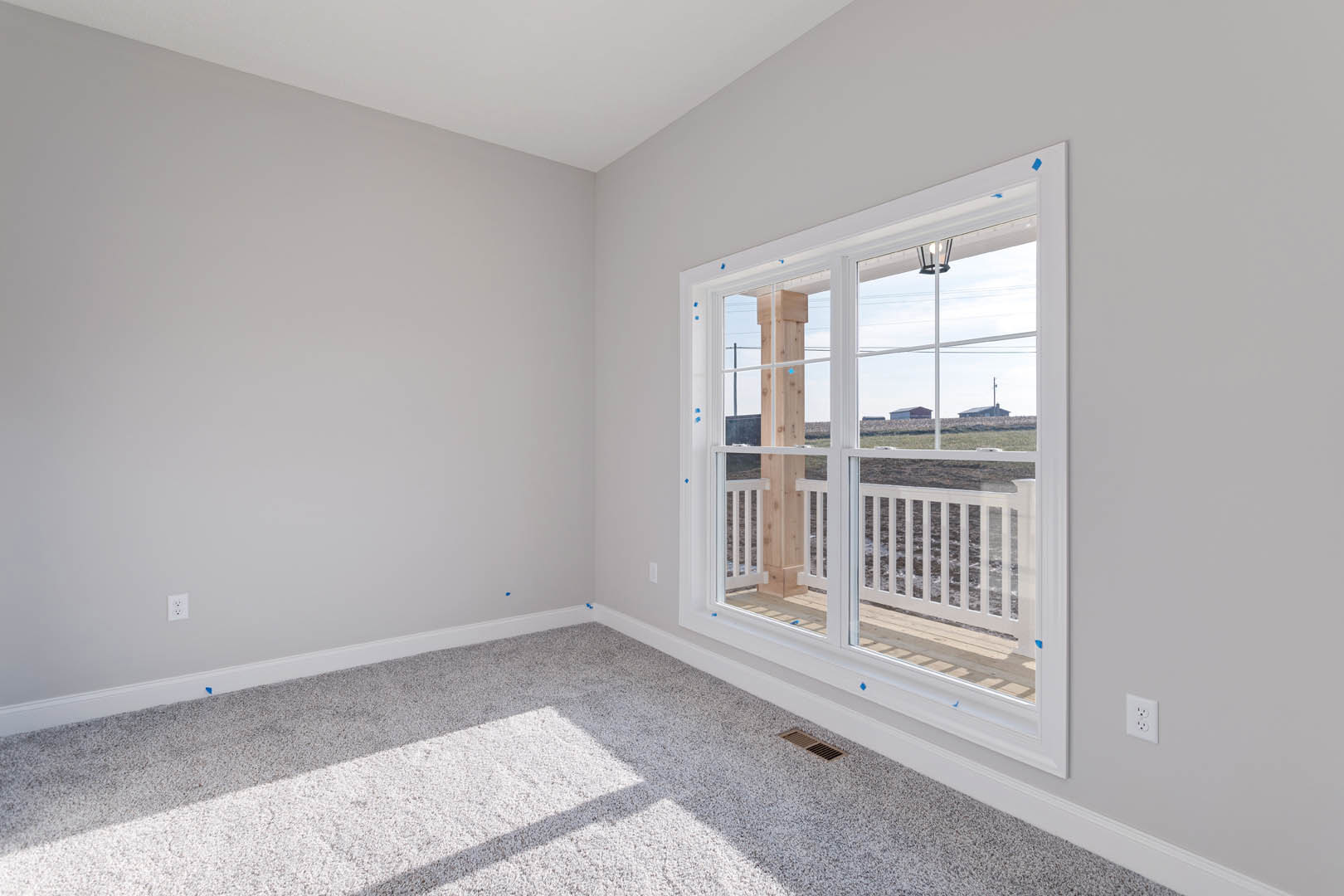 Carpeted bedroom with white walls, large window overlooking a field, and glass door opening to a balcony