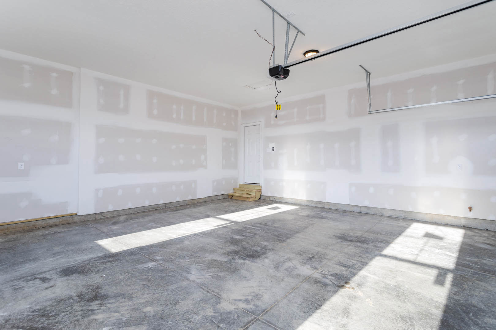 White walls, concrete tile floor, wooden staircase, modern light fixture, white door with black handle, black object with blue stripe