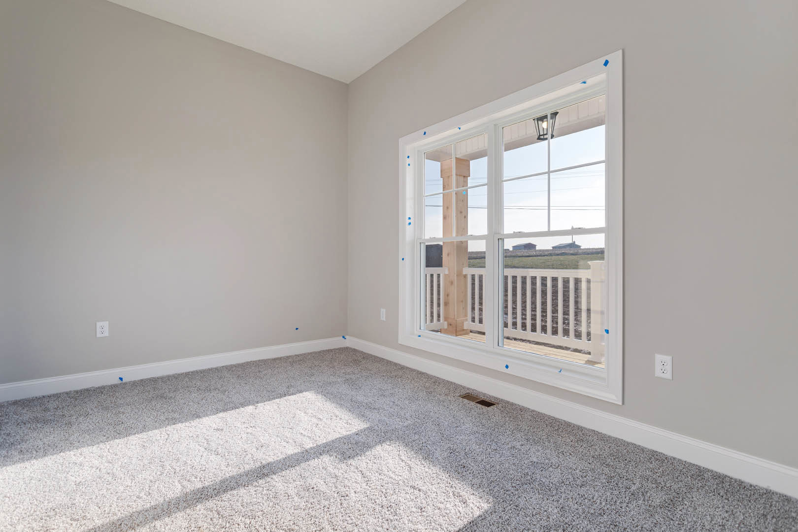 Carpeted room with a large window featuring a white railing outside, light fixture overhead, and sunlight casting a shadow on the floor.
