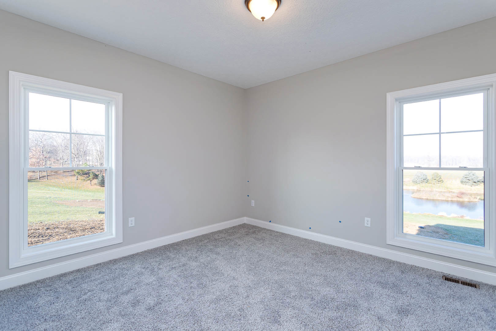Spacious carpeted room with large windows, white walls, ceiling light fixture, and views of trees and river outside
