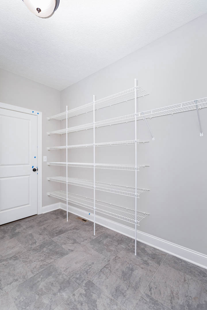 White built-in shelves against a plaster wall, white cabinet and door with blue tape, grey tile flooring, close-up of modern light fixture on ceiling