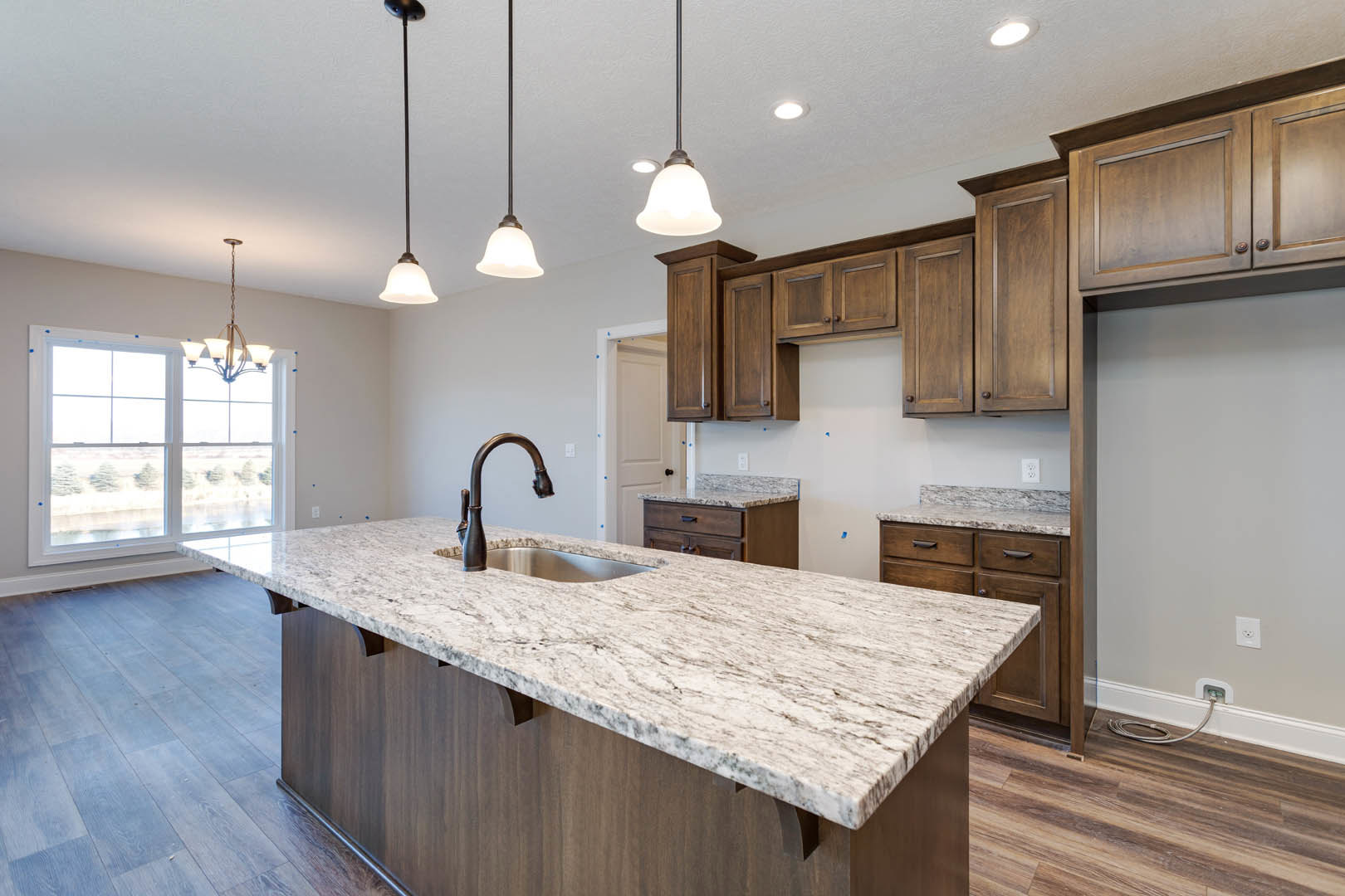 Marble kitchen island with built-in sink and chrome faucet, white cabinetry, pendant light fixture above, large window overlooking trees