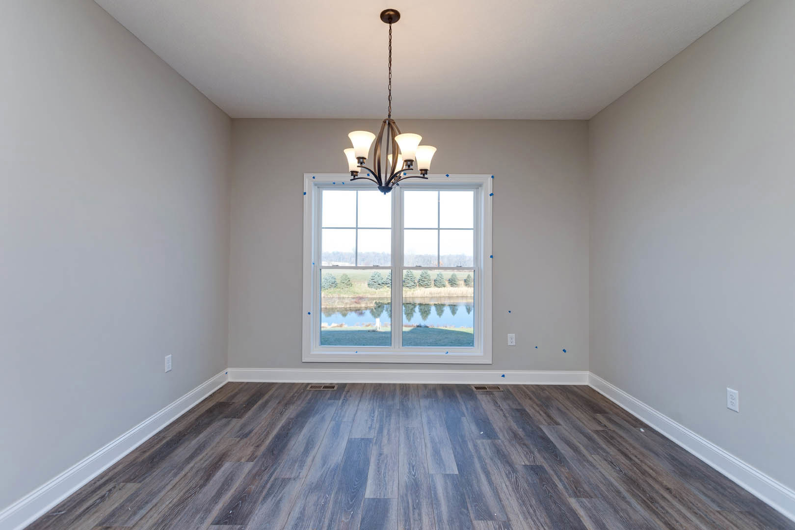 Lake view through large window, blue wood floor with vent, white plaster walls, decorative molding, chandelier and ceiling light fixtures