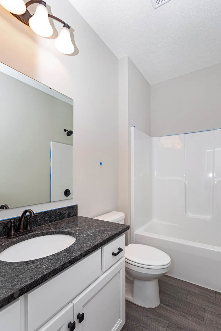 Modern bathroom featuring a white sink with black border, white toilet with closed seat, glass shower enclosure, wall-mounted faucet, and contemporary light fixture; blue trim