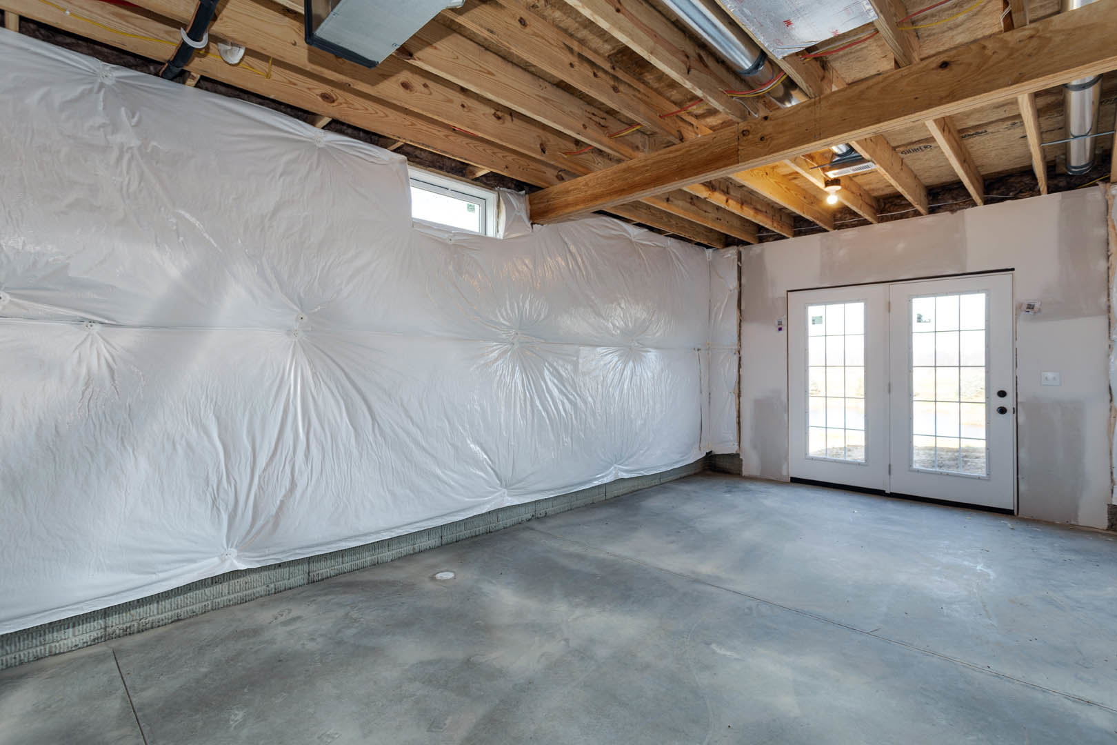 White double doors with glass panes set in a room featuring a white plaster wall, multi-pane window, and smooth white ceiling; wall partially covered in protective plastic.