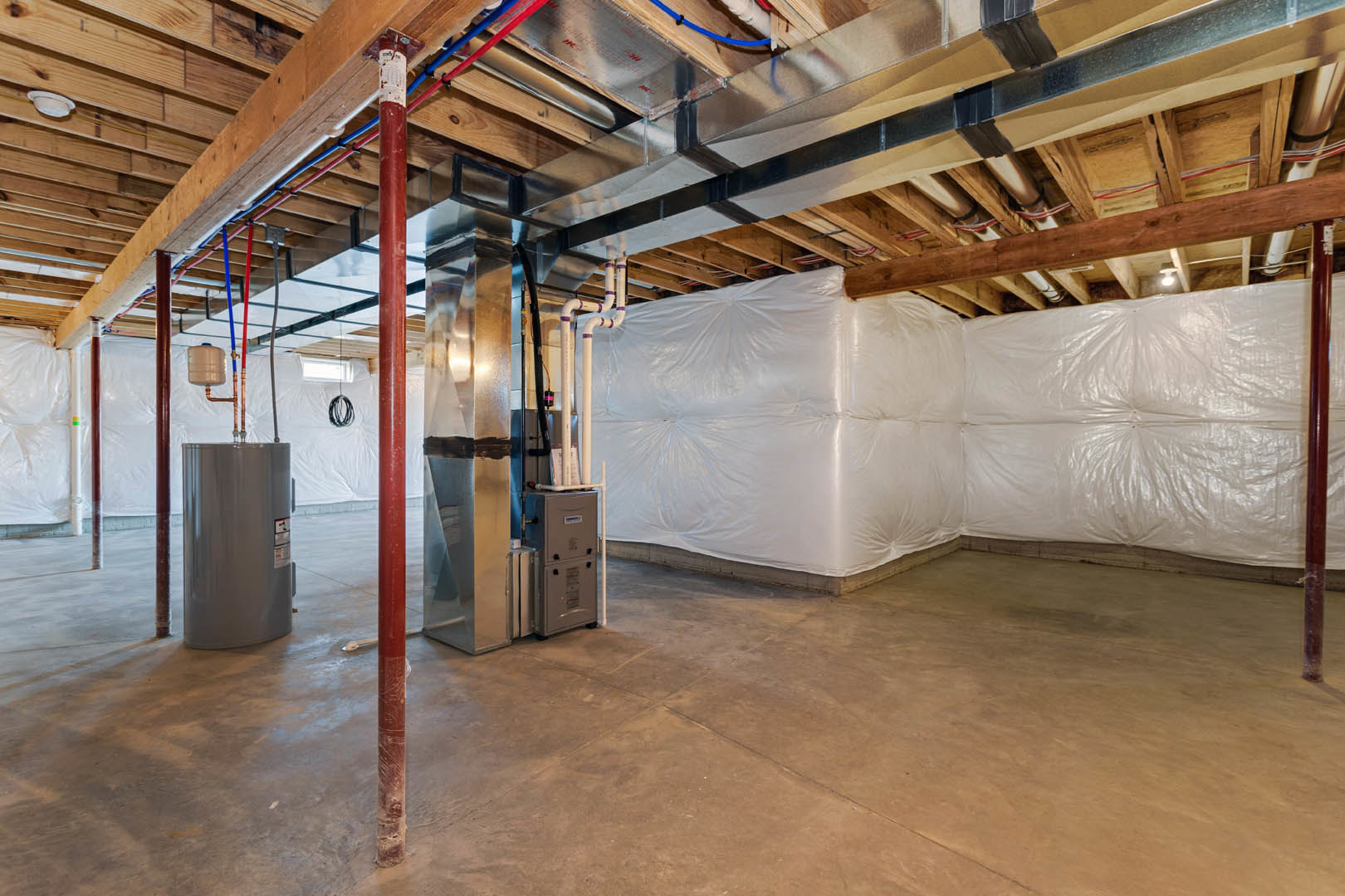 Spacious room featuring a large white wall, exposed wooden ceiling beams, metal boxes, silver cylinder, and visible pipes and insulation.