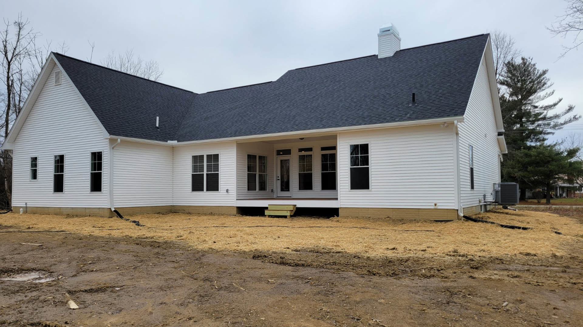 Two-story house with white siding, green porch trim, dirt yard, white-framed windows, and a covered entry.