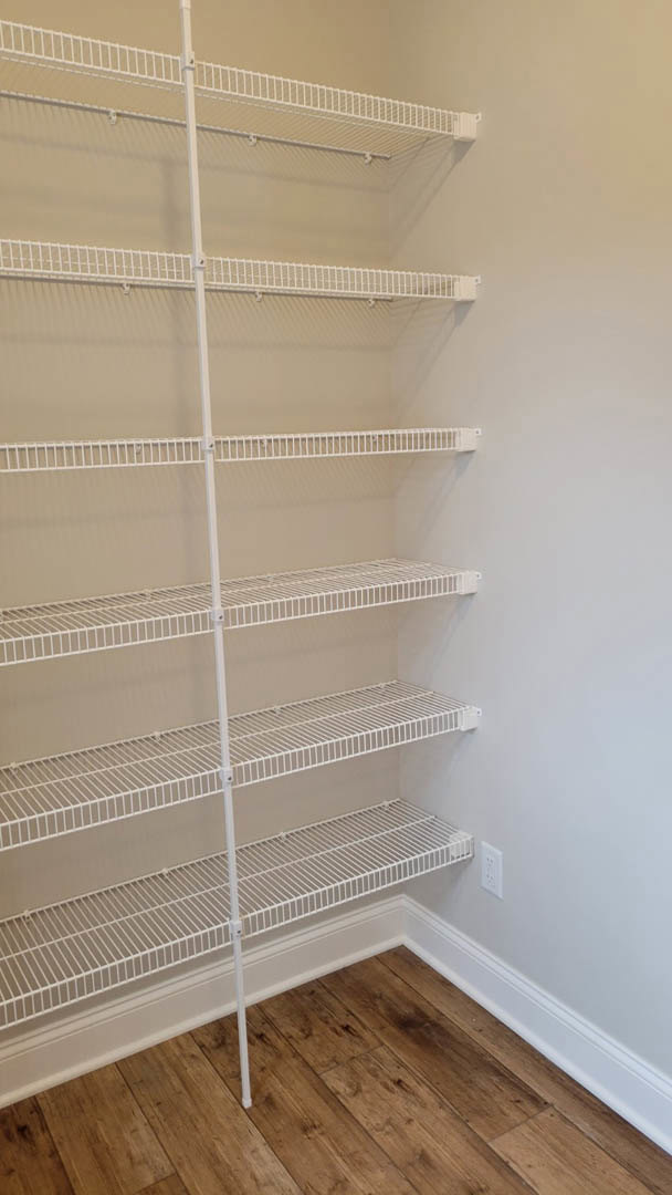 White built-in shelves against a light wall, wood flooring, white support pole, empty shelving, white crib near a closed door, white wire shelf adjacent to wood floor.