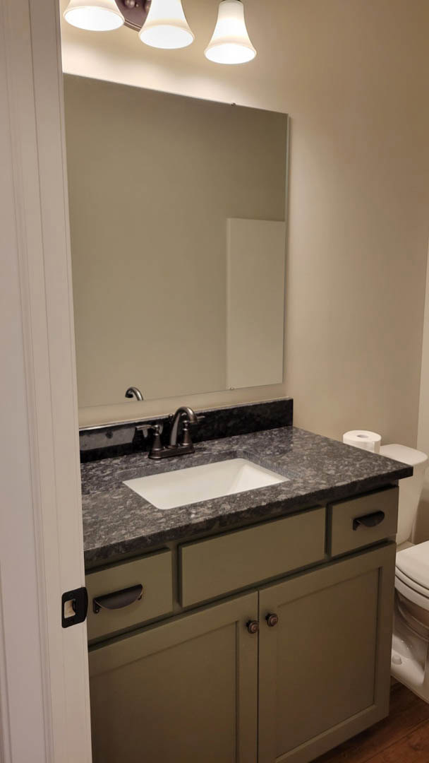 Modern bathroom with white rectangular sink, chrome faucet, brown wood cabinetry, stone countertop, large wall mirror, and neutral tile backsplash