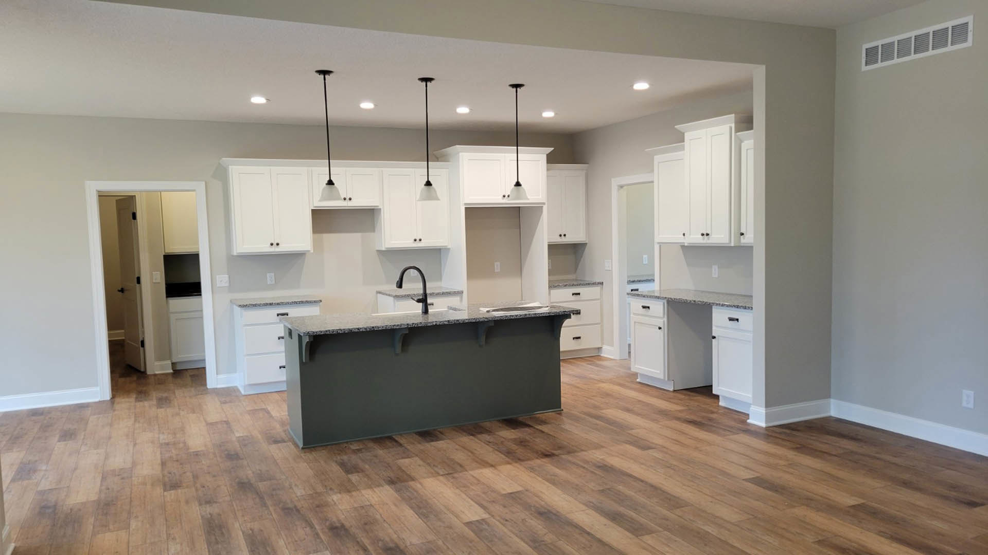 White kitchen cabinets and island with black faucet, wood flooring, black accent wall, vent, and door in background
