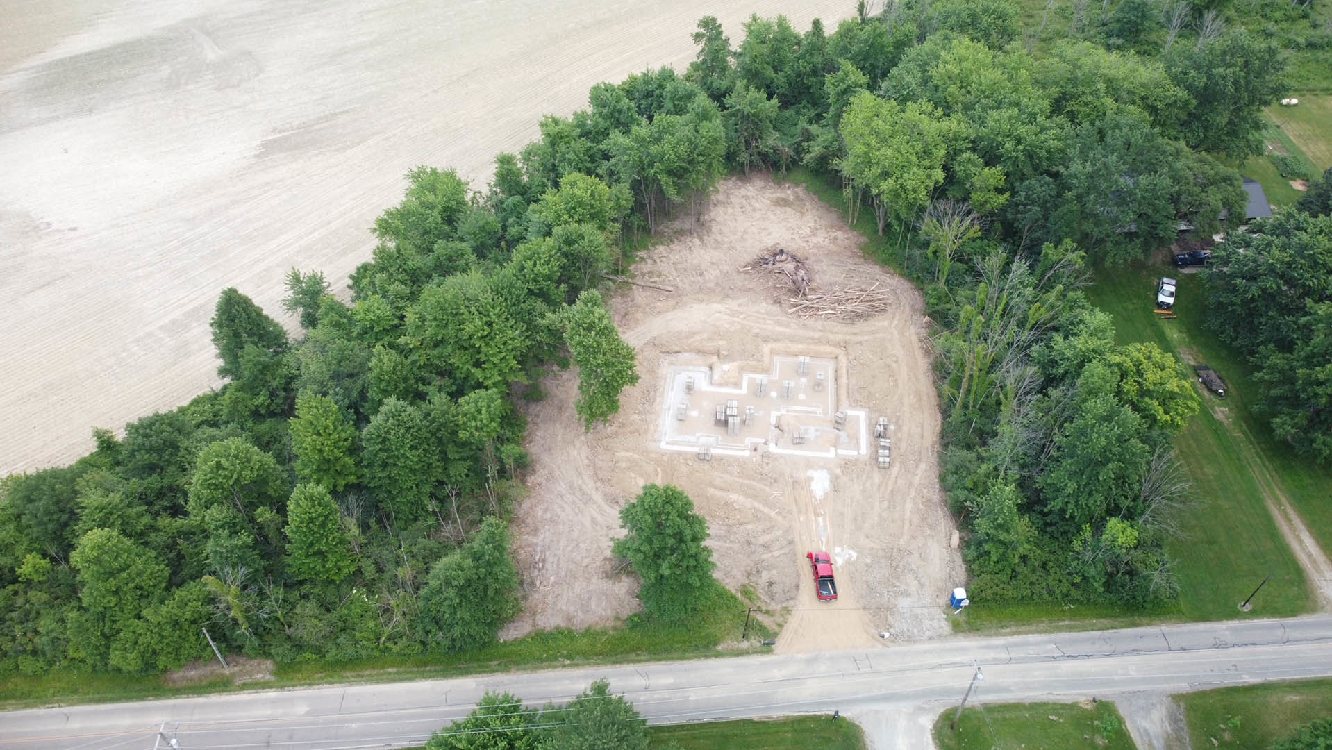 Aerial view of a residential construction site surrounded by trees and dirt, with patches of grass and landscaping visible