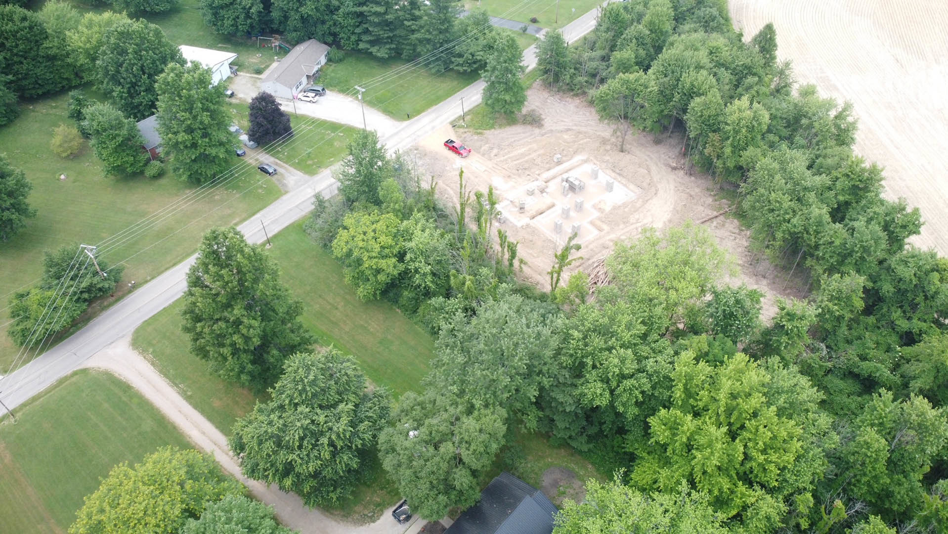 Aerial view of a residential neighborhood with mature trees, houses, grassy yards, and a playground featuring a slide; visible land lots and urban layout.