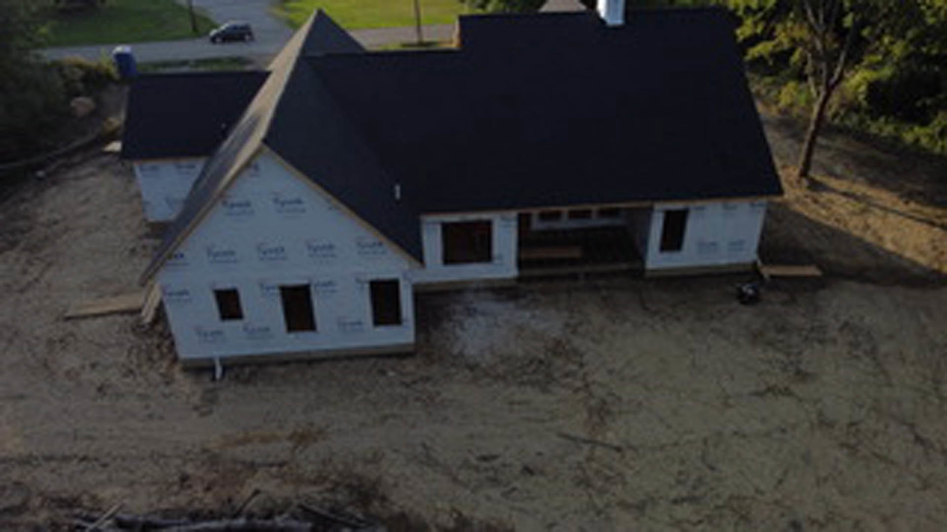 Two-story home with black shingle roof, white siding, large front windows, landscaped yard, and mature trees