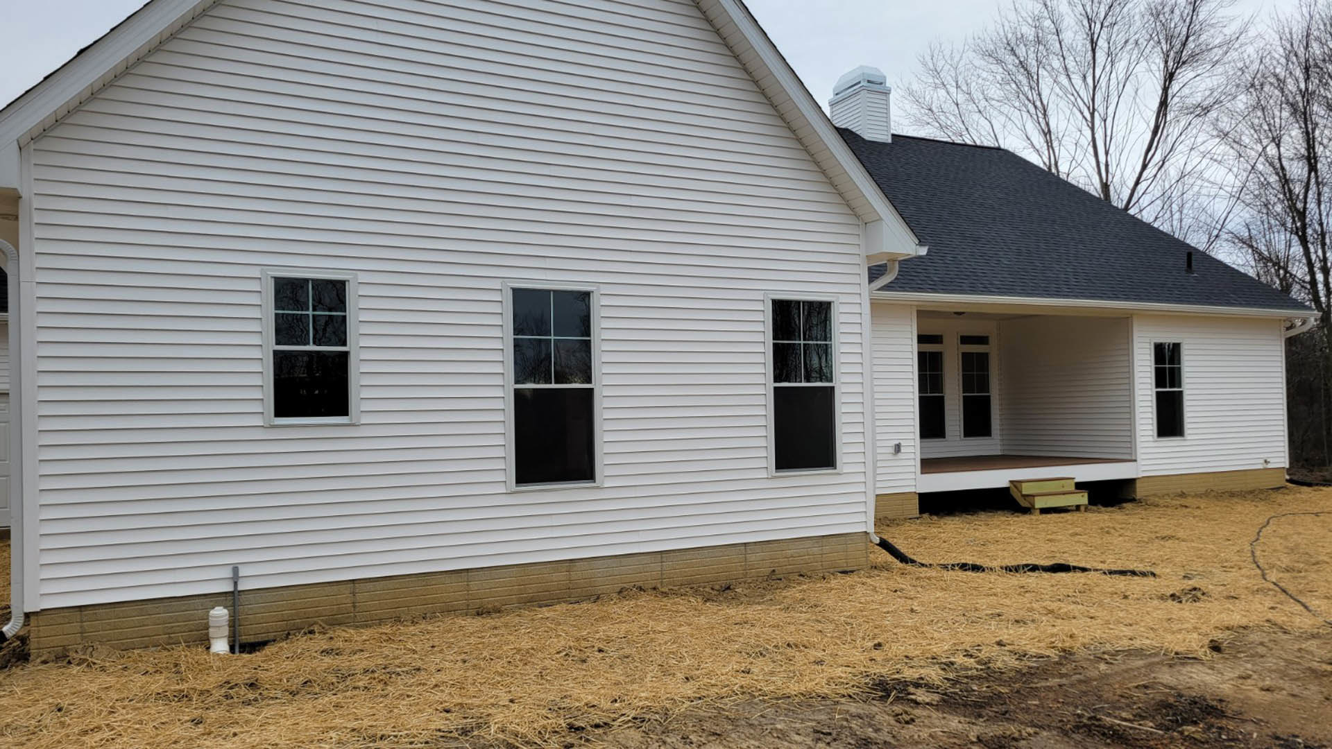 White house with two windows, black screen and white frames, black door, green yard with a mature tree, light siding, blue sky overhead