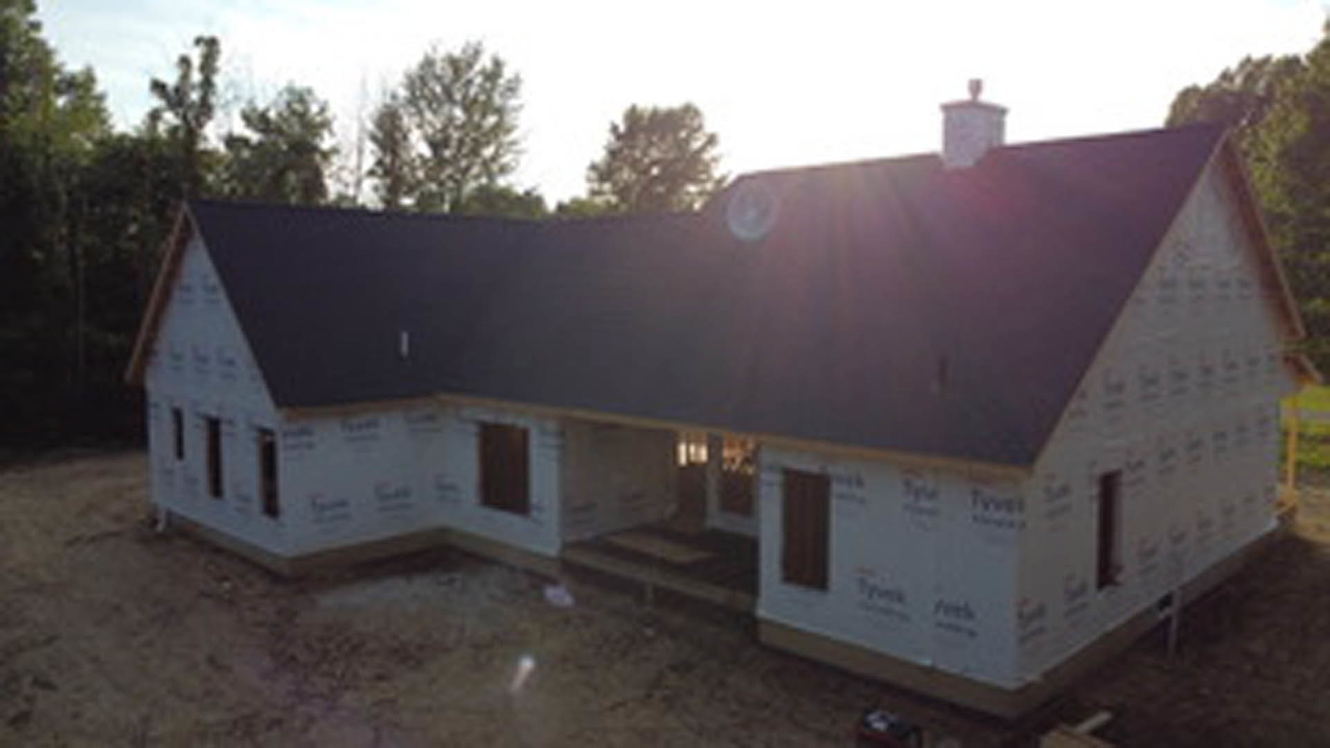 Partially built house with black shingle roof, exposed framing, and surrounding trees in the background