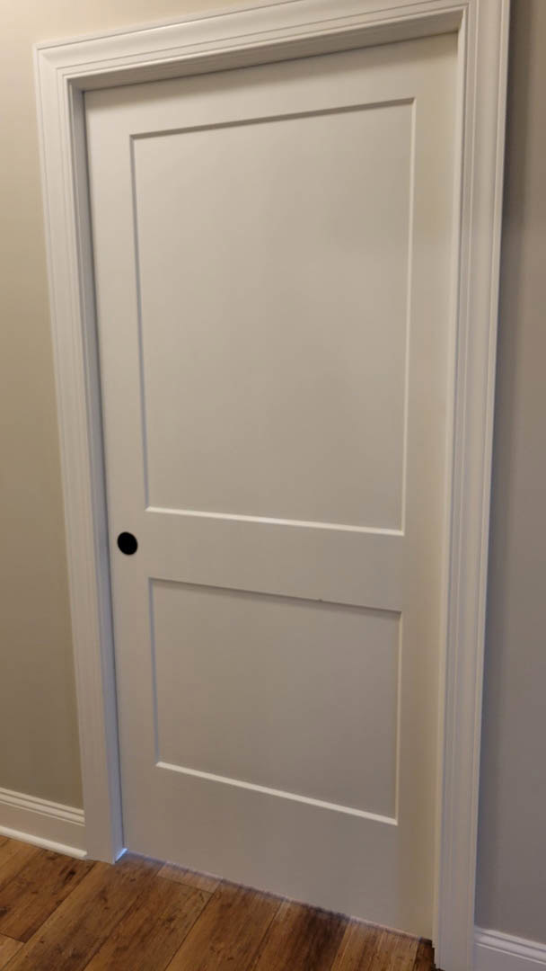 White door with matte black handle, wood floor, and smooth white wall in a modern entryway