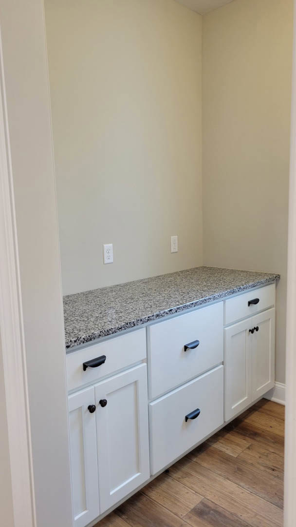 White countertop with integrated sink, white cabinets featuring silver handles, light wood flooring, and tiled backsplash in a modern kitchen.