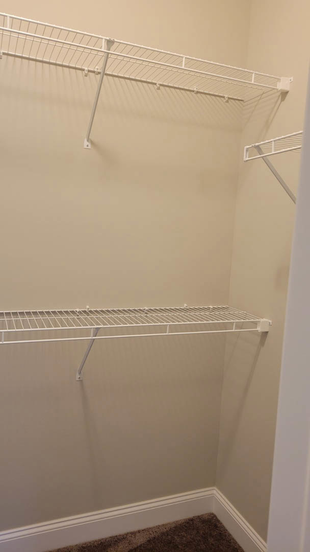 White wire shelving with metal bars and hooks installed in a closet with carpeted flooring and plaster walls.