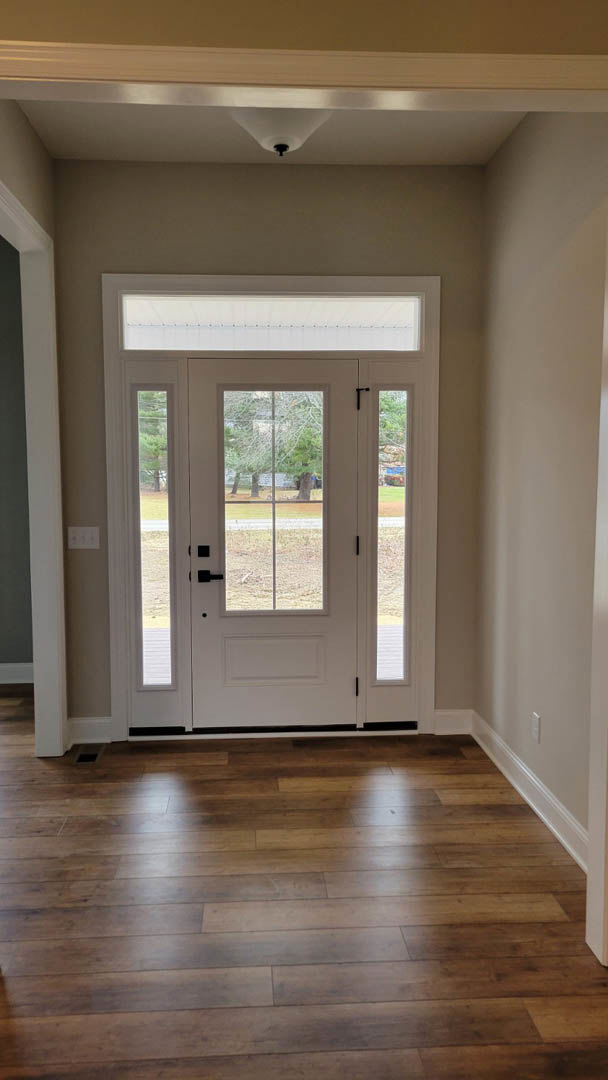 White door with glass panes, wood flooring, white walls, window showing trees, white light fixture with black knob