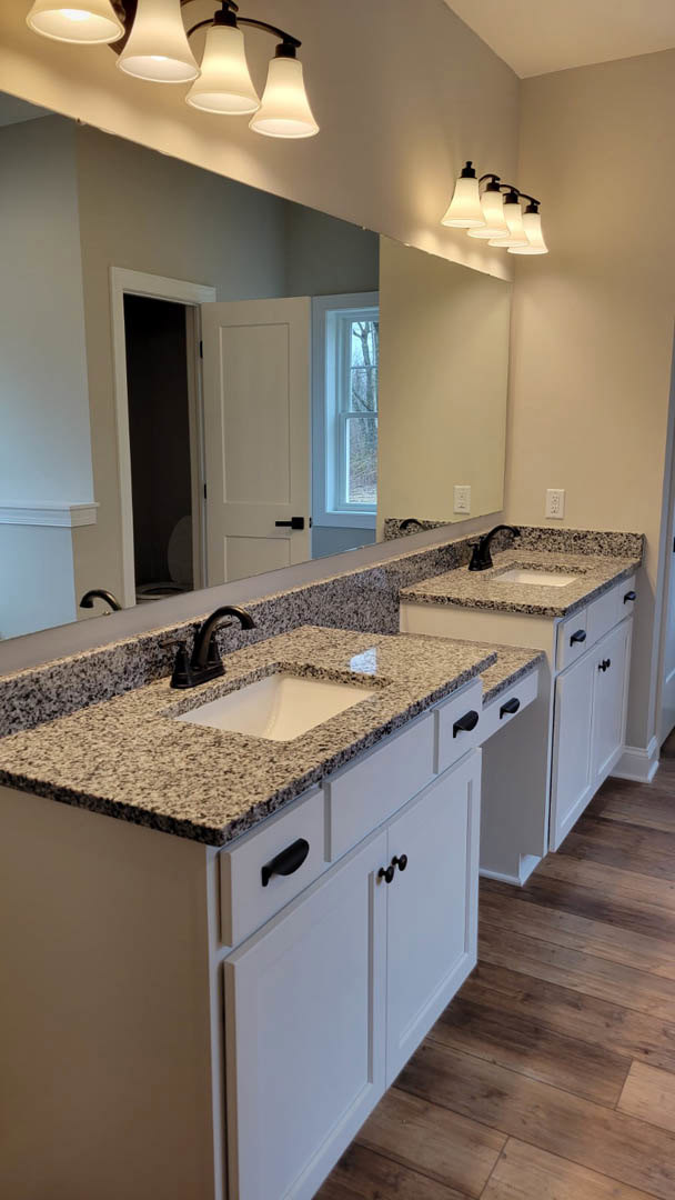 Bathroom with double sinks set in a white countertop, expansive wall mirror above, modern faucets, and cabinetry below.