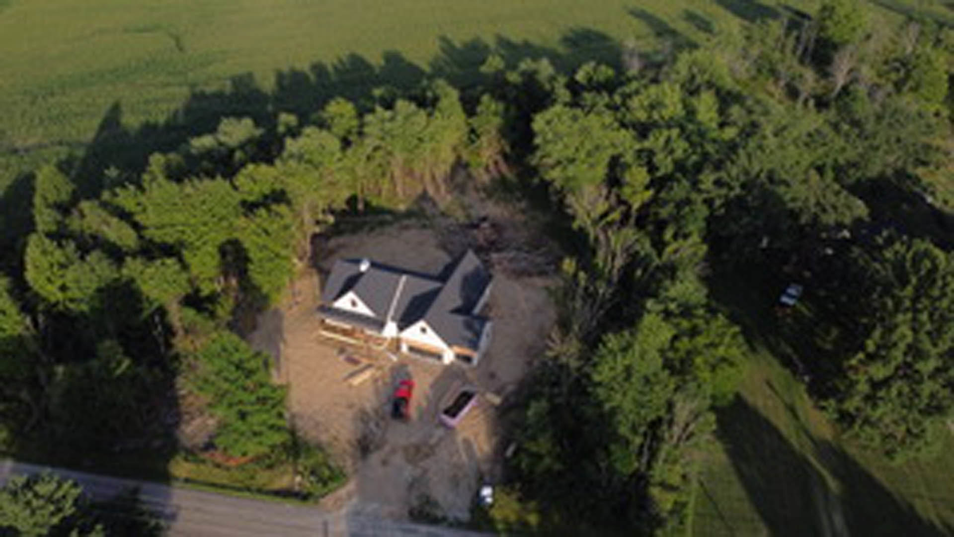 Modern two-story house with gray roof and large windows, nestled among tall trees and lush green grass, viewed from above