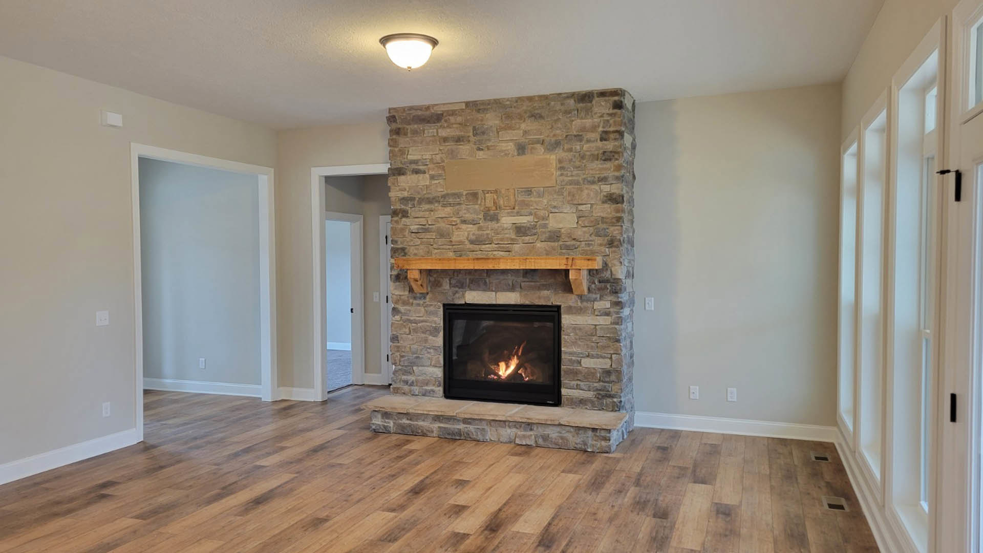 Brick fireplace with wood mantel shelf, white wall frame above, wood beam accent, wall-mounted light fixture, wood laminate flooring