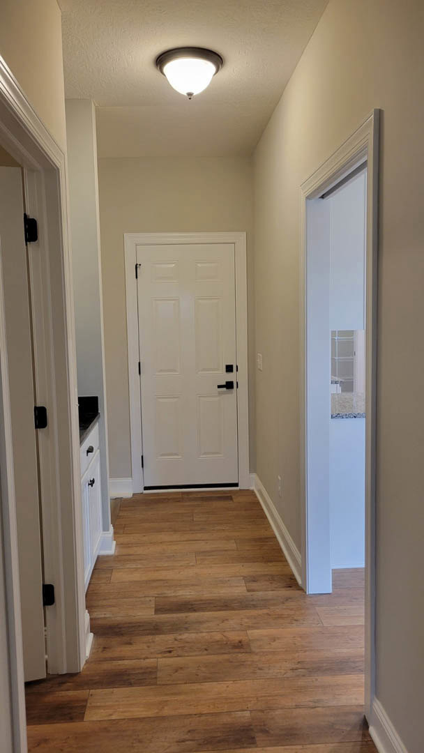 Hallway with white paneled doors featuring black handles, wood plank flooring, white walls, and a ceiling light fixture