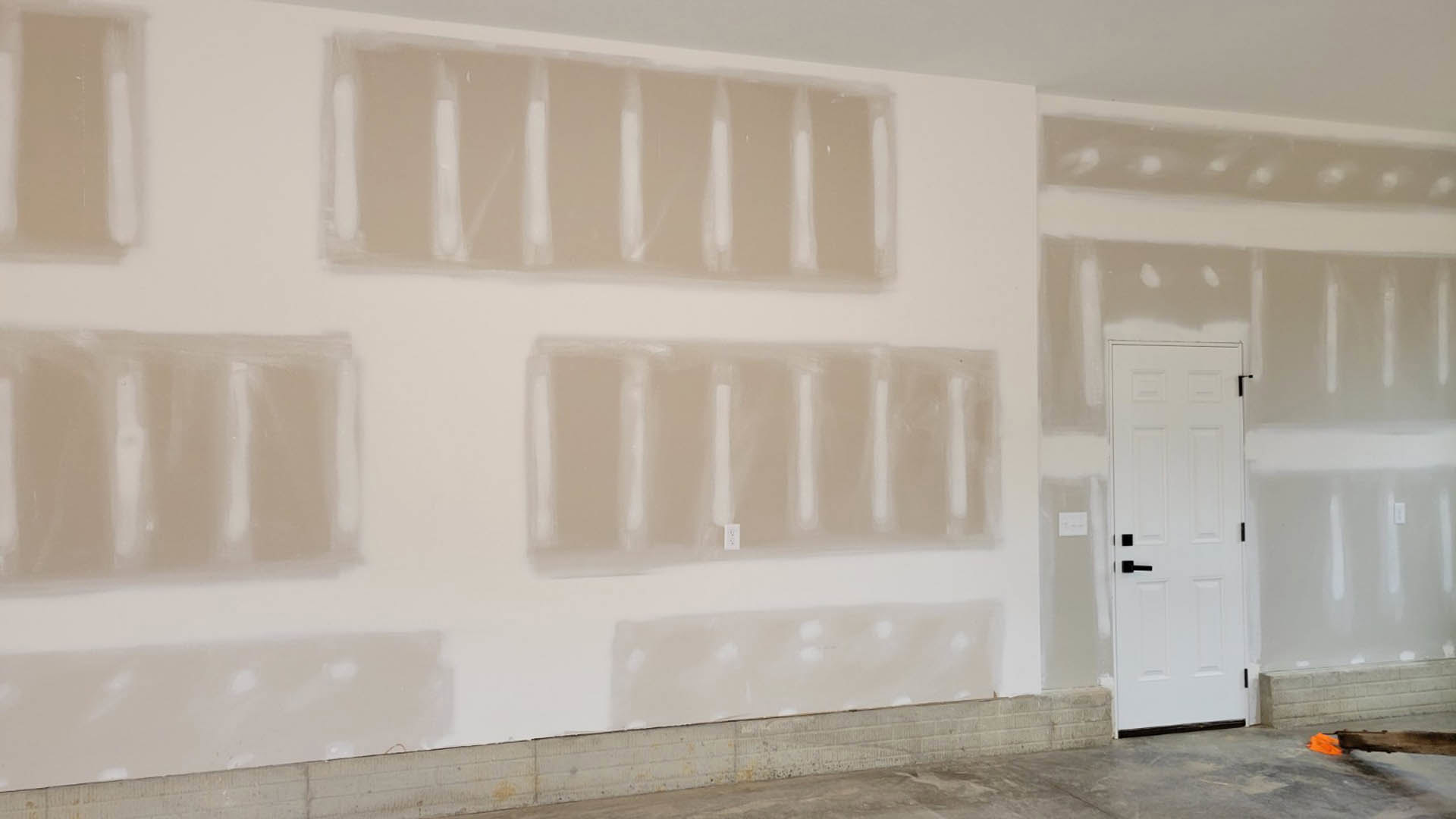 White painted wall with a white door featuring a black handle, light switch, and a person standing nearby; close-up of a plastic bag on the floor.