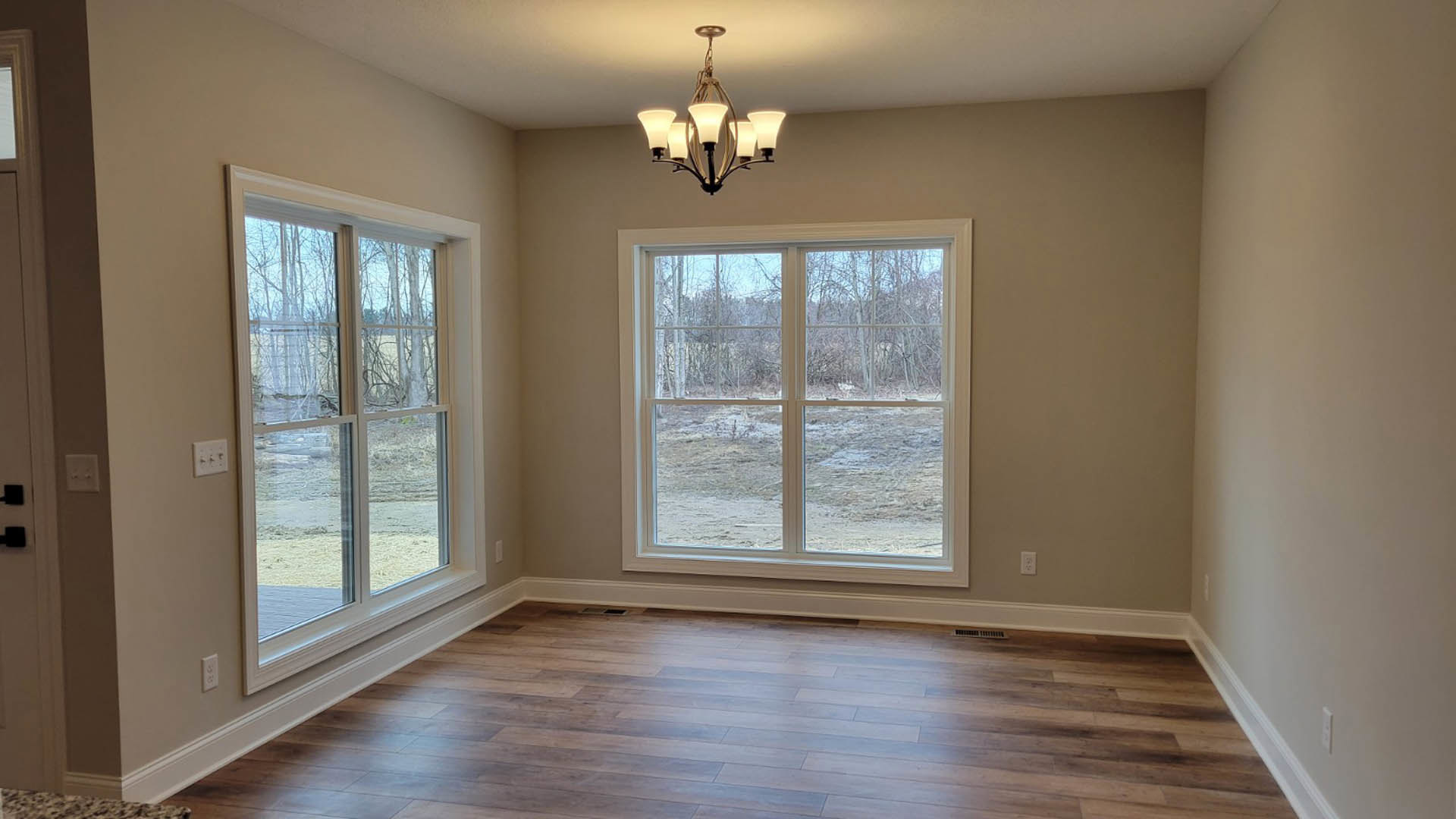 Spacious room featuring large windows, five-light chandelier, wood flooring with floor vent, plaster walls, and light switch near entry.