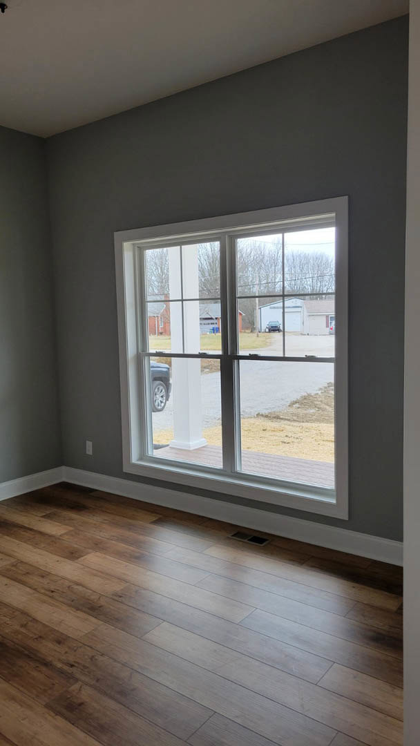 Large window with white trim overlooking a parked car and garage, wood laminate flooring, white walls