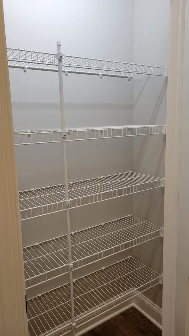 White closet with multiple white wire shelves, wood flooring, and a white metal ladder mounted on the wall.