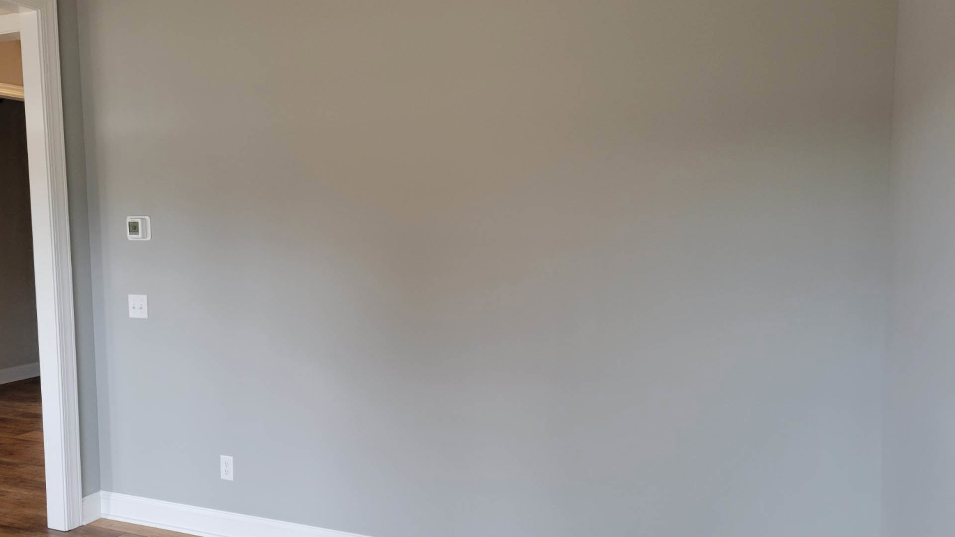 White plaster wall with white ceiling, wood floor, white door frame, square window, and wall switch with two black buttons