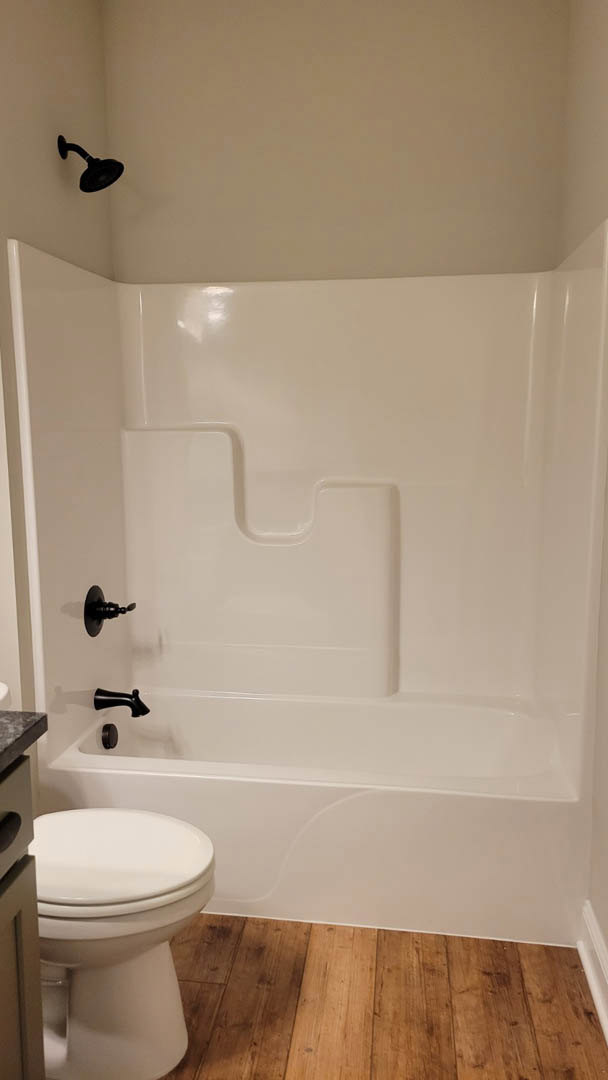 Freestanding white bathtub with matte black faucets, adjacent white sink, wood flooring, and white walls in a modern bathroom