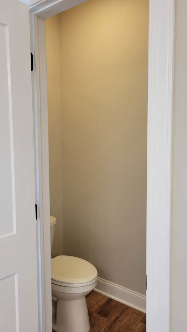 White toilet with closed lid on wood flooring, white baseboard, and light-colored tile walls in a residential bathroom.