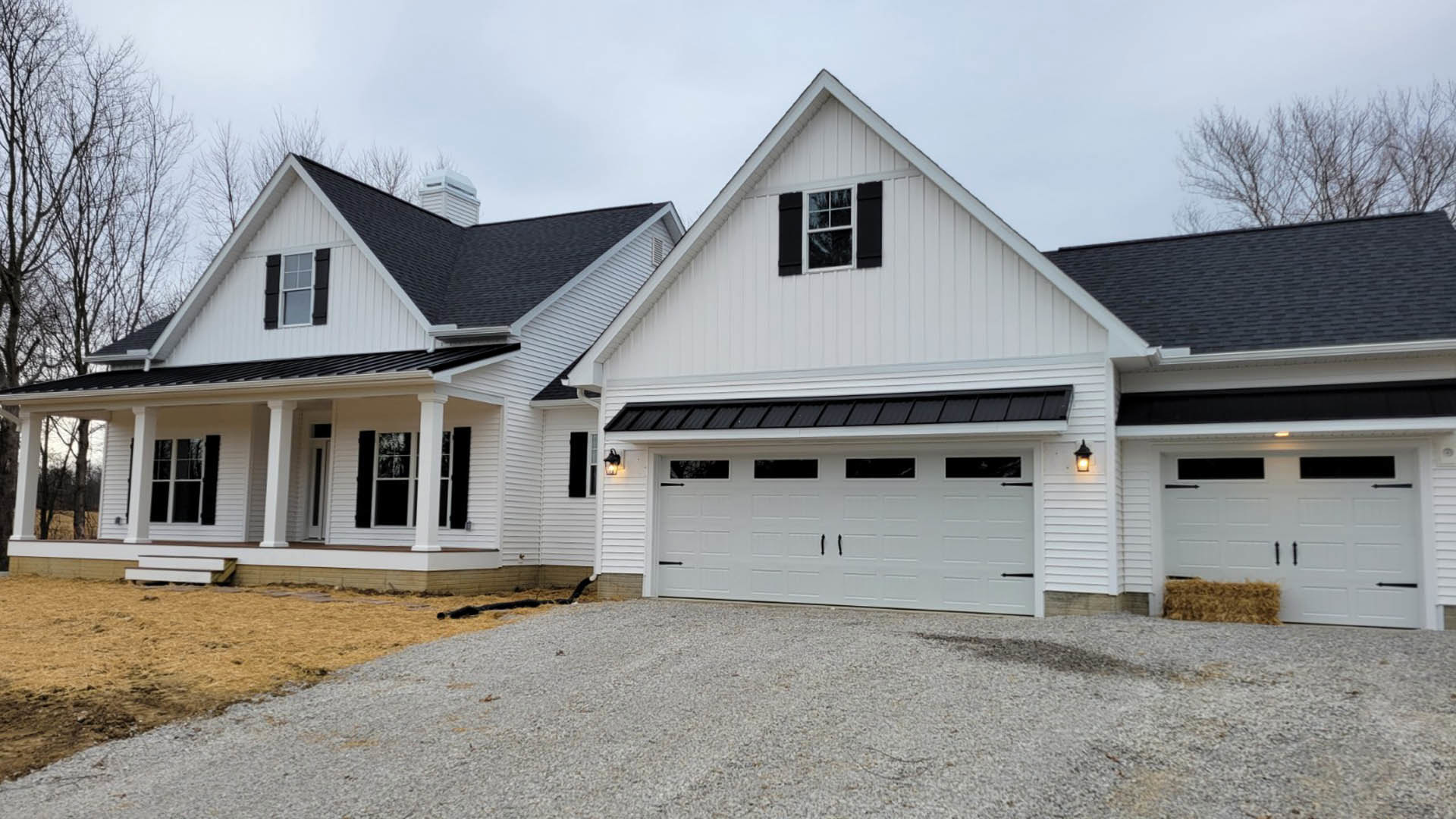 Two-story home with light siding, black window shutters, attached garage, gravel driveway, white garage door, and gabled roof.