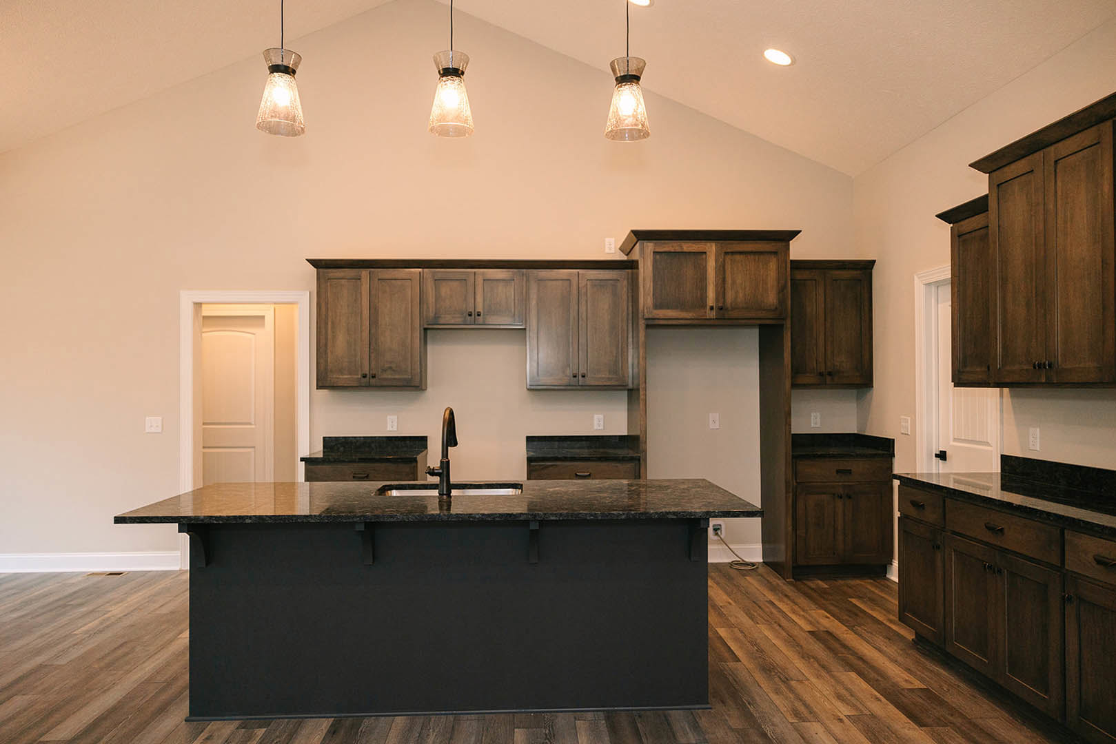 Kitchen featuring a black island with matching countertop and sink, wooden floors, white cabinetry, close-up views of wooden cabinets, a white door illuminated by overhead