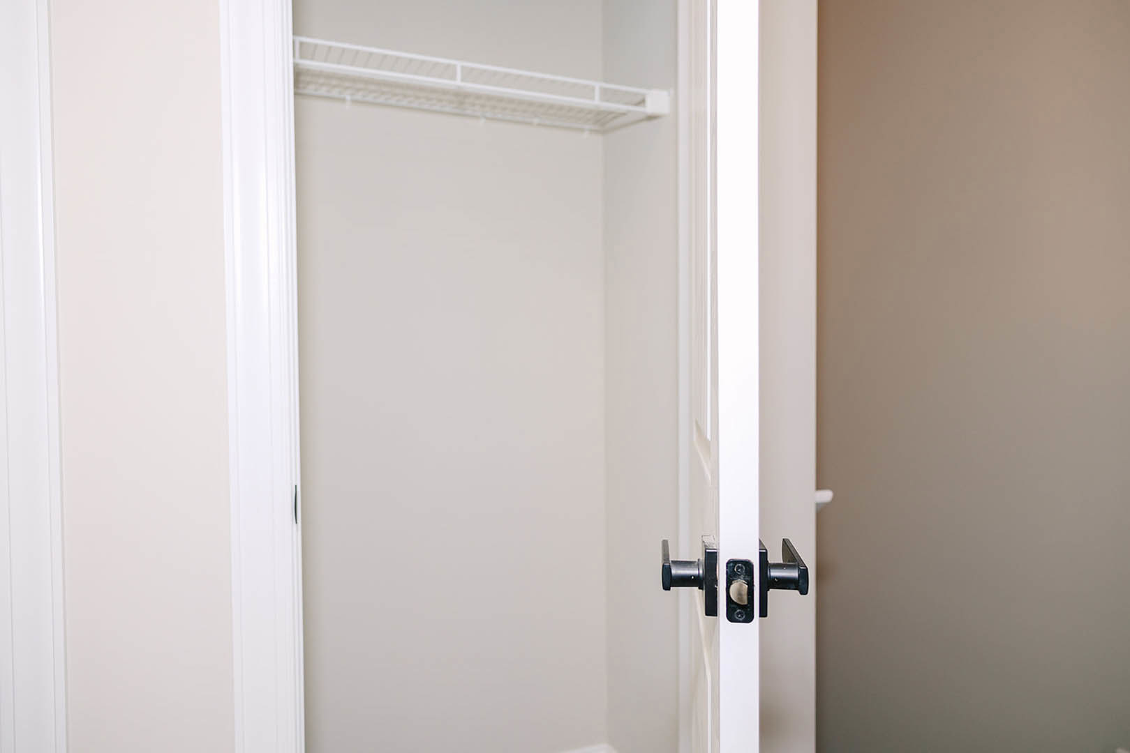 White door with silver handle open to a closet, white shelving mounted on white walls, black object in corner.