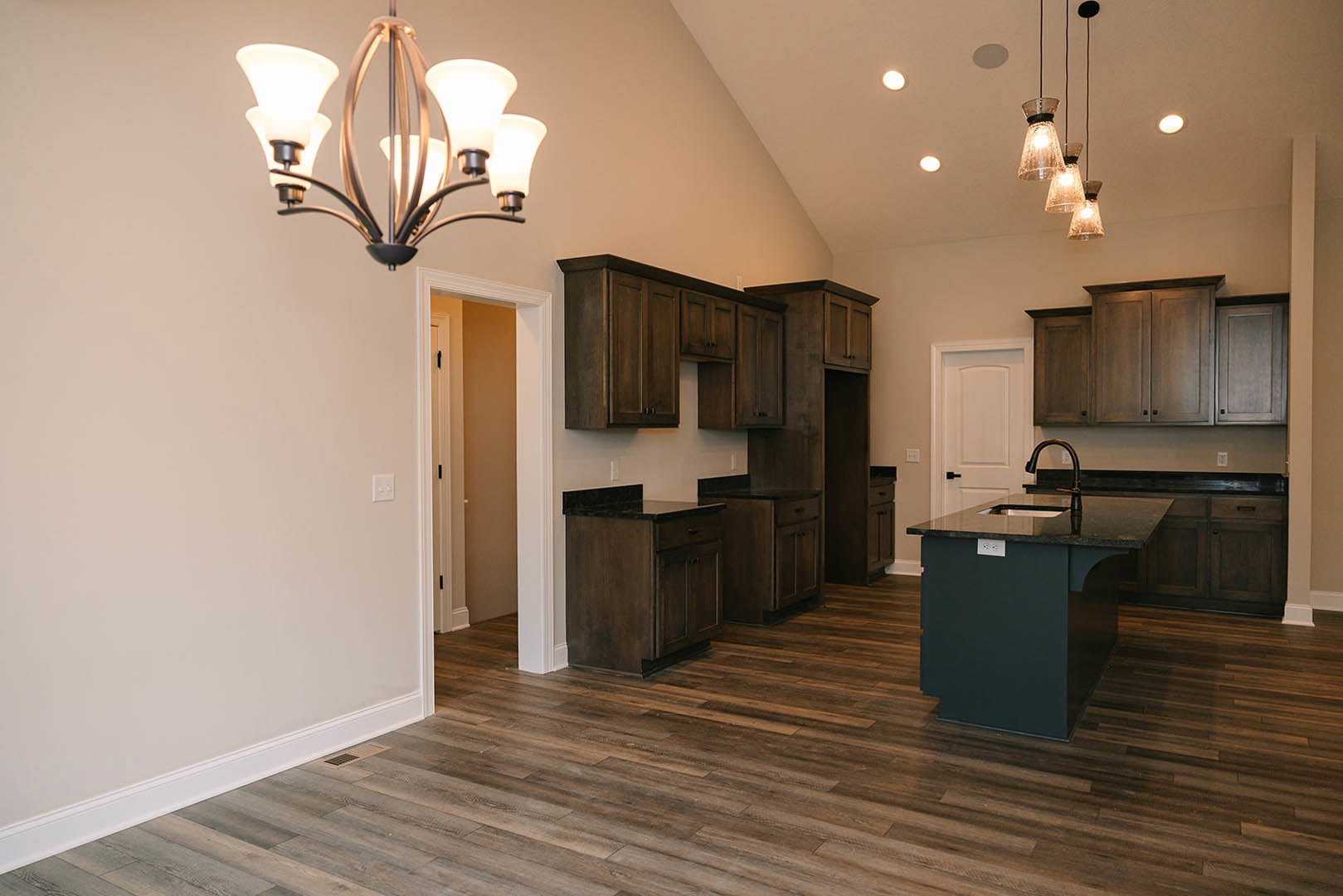 Kitchen with wide plank wood flooring, black countertop and sink, white cabinetry, and a decorative chandelier hanging from the ceiling