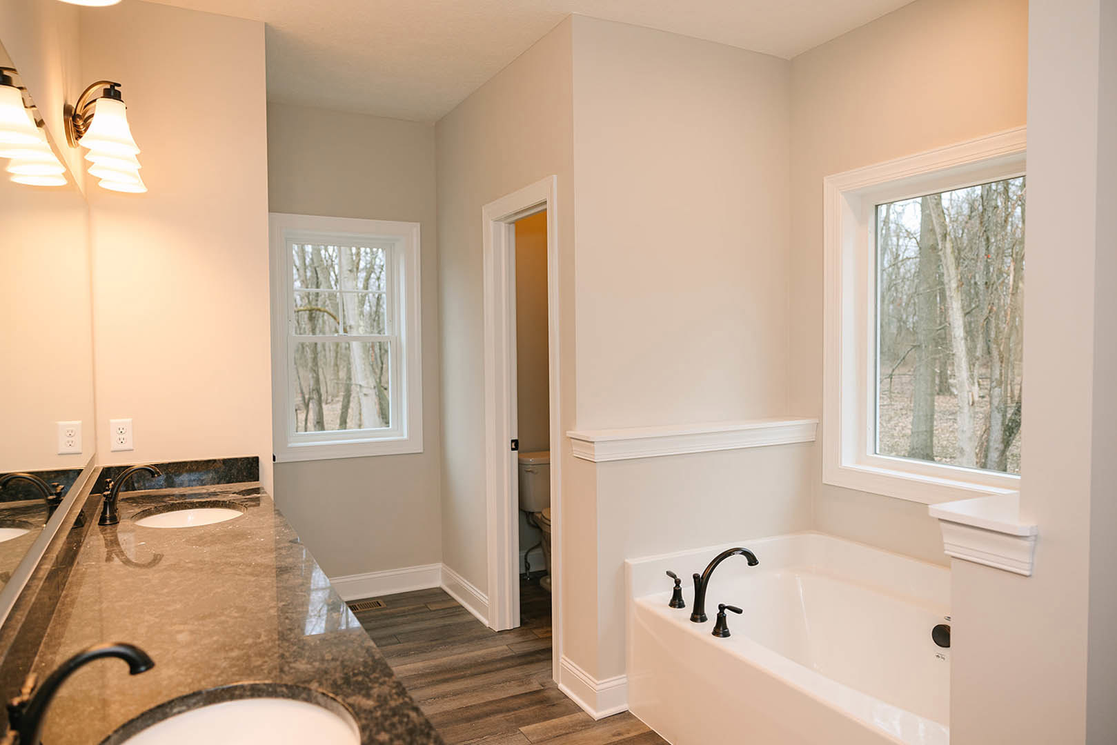 Bathroom featuring marble countertops, freestanding tub with chrome faucets, large window overlooking trees, tiled walls, modern light fixture, and wall-mounted mirror