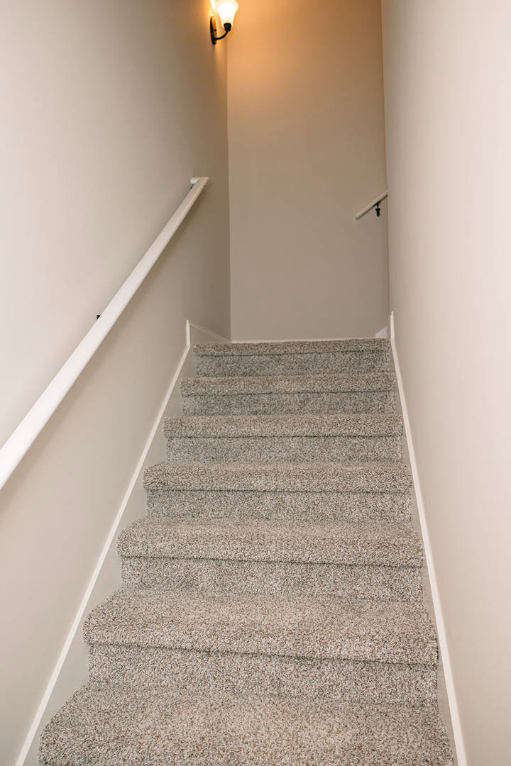 Carpeted staircase with white railing, white plaster walls, ceiling light fixture, and tile flooring at the base